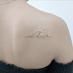 the back of a woman's shoulder with a small wave tattoo on her left shoulder