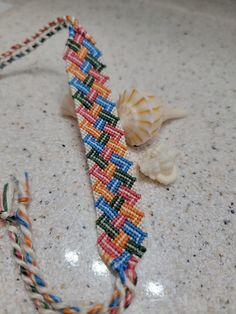 a colorful beaded bracelet sitting on top of a counter next to a seashell