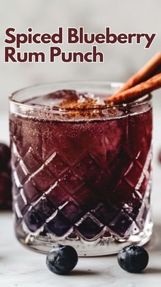 a close up of a drink in a glass on a table with blueberries and cinnamon sticks