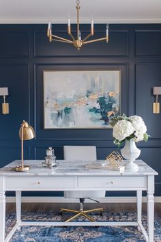 a white desk with gold accents in a blue and white office space by the painting on the wall