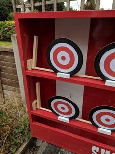 a red book shelf with three target plates on top and two wooden sticks sticking out of it