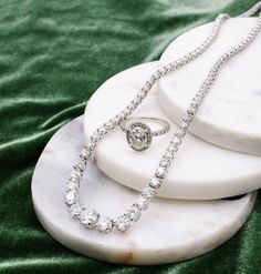 a necklace and ring sitting on top of a white marble stand next to a green cloth