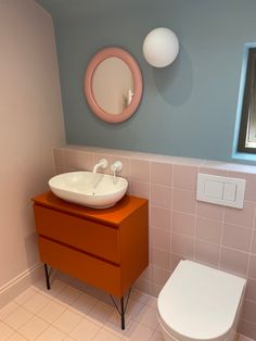 a white toilet sitting next to a sink in a bathroom under a round mirror on the wall