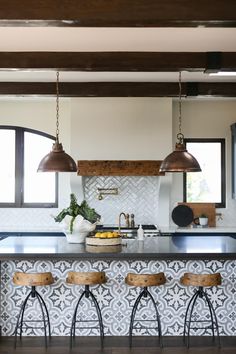 a kitchen with three stools in front of an island and two lights hanging from the ceiling