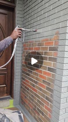 a man is using a hose to spray paint on a brick wall in front of a door