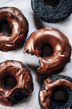 four chocolate donuts with frosting on top of a white countertop next to each other