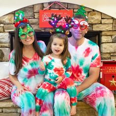 a man and woman wearing christmas themed pajamas with their child in front of a fireplace