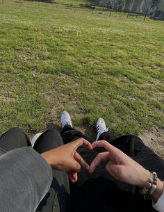 two people sitting on the ground making a heart shape with their hands in front of them