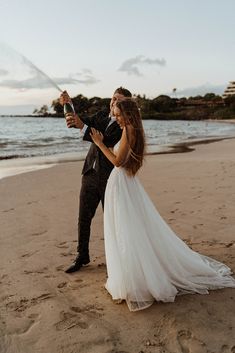 a bride and groom on the beach holding an umbrella