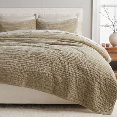 a bed with a white headboard and beige quilted bedspread in front of a window