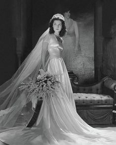 a woman in a wedding dress and veil poses for the camera, holding a bridal bouquet