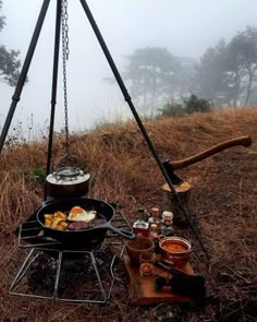 an outdoor grill with food on it in the foggy field next to some trees