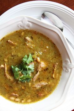 a white bowl filled with green soup and garnished with cilantro leaves