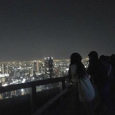 three people standing on top of a building looking at the city lights in the distance