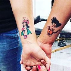 two people holding hands with tattoos on their arms and one has a cartoon character on the wrist