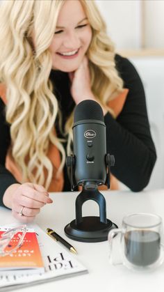 a woman sitting at a table with a microphone in front of her and a cup of coffee