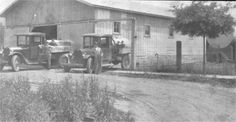 an old black and white photo of two men standing in front of a barn with trucks