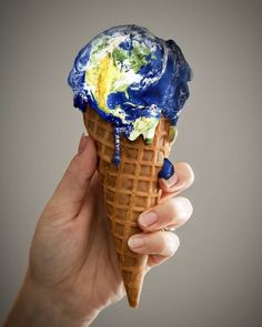 a hand holding an ice cream cone with the earth on top