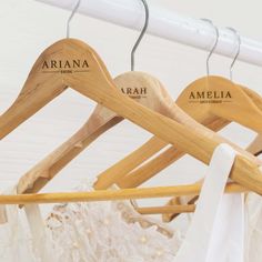 three wooden clothes hangers with names on them and white dresses hanging in the background