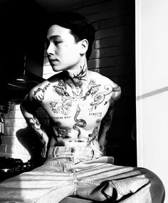 a man with tattoos on his body sitting in front of a stove and looking off into the distance