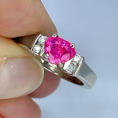 a person holding a ring with a pink stone in it's center and two diamonds on the side