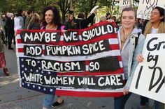 some people holding signs and standing on the street with one person holding a sign that says maybe we should add pumpkin spice to racism so why women will care