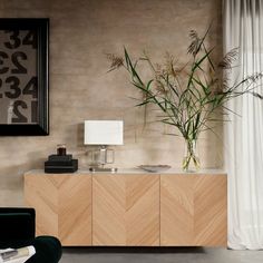 a plant in a vase on top of a wooden sideboard next to a window