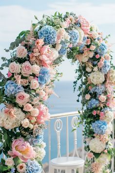 an outdoor wedding arch with flowers and greenery on the top of a balcony overlooking the ocean