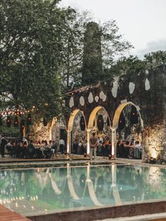 an outdoor wedding reception next to a swimming pool at dusk with string lights and hanging decorations