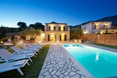 an empty swimming pool in front of a house at night with lawn chairs around it