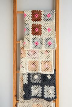 three crocheted squares are hanging on a wooden ladder, and one is made with yarn