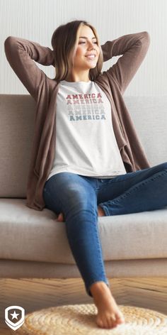 This pin is an image of a smiling, attractive woman reclining on a couch. She's wearing a sweater with Patriot Depot's T-Shirt under it. The shirt has America written 5 times. The top is red, below that is light red, the middle is white, below that is light blue, and the bottom "America" is blue.The shirt is a light grey blue. This image suggests you wear the outfit with blue jeans. On the bottom left is Patriot Depot's logo. American Pride