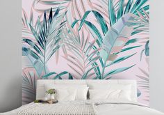 a white bed sitting next to a pink wall with palm leaves on it and a potted plant