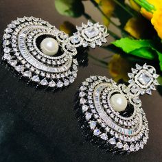 These are a beautiful pair of Earrings made with American diamonds. These chandbali work well with everything and are made with a gold base. They have white American diamond stones and White semi-precious stones in a diamond pattern that will go well with every outfit in your closet. Best for gifting or for personal use, wear it to any occasion and be the spotlight. Eye-catching and unique jewelry that will set you apart. Gift this piece to a loved one, and see their face light up with joy. Silver Chandbali Danglers With Elegant Design, Elegant White Danglers With Stone Work, Elegant Stone Work Chandbalis For Diwali, White Stone Work Earrings For Formal Occasions, Elegant White Kundan Earrings, Elegant Bridal Earrings With Stone Work In Cubic Zirconia, Elegant White Chandelier Earrings With Stone Work, Diamond Chandbali Bridal Earrings For Wedding, Dazzling Diamond White Chandelier Earrings