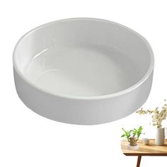 a white bowl sitting on top of a wooden table next to a potted plant