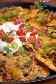 nachos with bacon, cheese and tomatoes in a skillet topped with sour cream