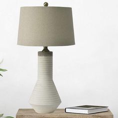 a table lamp sitting on top of a wooden block next to a book and potted plant