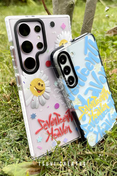 two cell phones sitting on top of each other in the grass with graffiti written on them