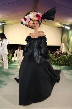 a woman in a black dress with flowers on her head walking down the catwalk