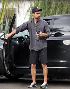 a man standing in front of a car with his hand on the open door handle