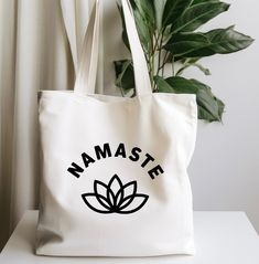 a white tote bag with the words namaste on it next to a potted plant