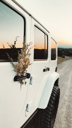 a white jeep parked on the side of a dirt road with flowers growing out of it