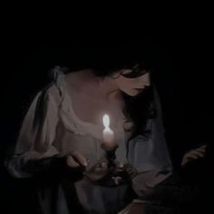 a woman holding a lit candle in her right hand and looking down at the ground