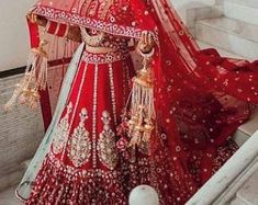 a woman in a red and gold bridal gown standing on stairs with her veil draped over her head