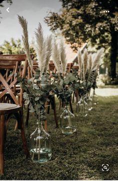 an outdoor ceremony setup with chairs and vases filled with flowers, greenery and feathers