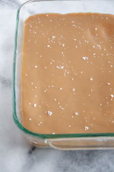 a square glass dish filled with peanut butter and brown sauce on a marble counter top