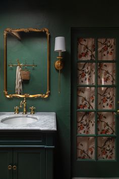 a bathroom with green walls and a gold framed mirror on the wall next to a sink