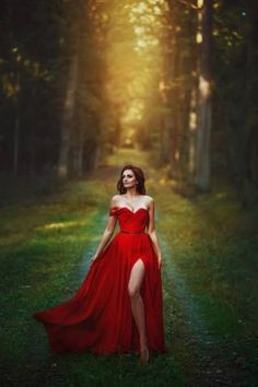 a woman in a red dress is walking through the woods