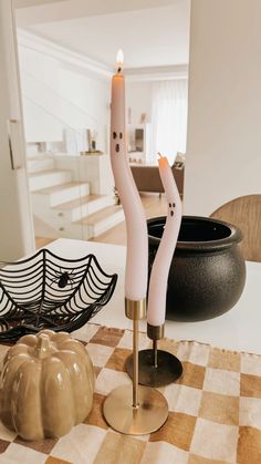 two candles sitting on top of a table next to a black bowl and pumpkins