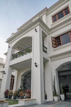 a large white house with lots of windows and plants on the front porch, along with two balconies